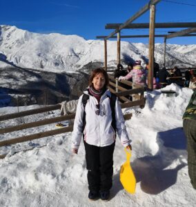 Paola Barberis lächelnd im Schneegebirge, mit einem schwarz-weißen Skianzug und einem gelben Schneerutscher in der Hand. 